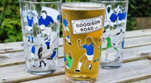 Three Everton Player pint glasses on a wooden table, with the middle glass filled with beer showing the iconic Goodison Road L4 artwork, ideal for Everton Father's Day gifts.