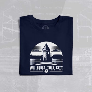 The image shows a folded navy blue T-shirt with a white graphic design on the front. The design features a stylized illustration of Goodison Park, Everton Football Club's historic stadium, with its iconic Archibald Leitch latticework and a prominent tower structure. Above the stadium illustration, there is a semi-circle with a triangular shape at the top, resembling a rising sun or a badge. Below the illustration, the text reads: "WE BUILT THIS CITY ORIGINALS SINCE 1878." The word "ORIGINALS" is in bold, and "SINCE 1878" is smaller, with a small Everton FC crest (a shield with the initials "EFC" and a tower) placed between the two phrases. In the background, there is a faint blueprint or architectural drawing of Goodison Park, with text such as "NEW GRAND STAND WEST" and "THE EVERTON FOOTBALL CLUB LTD" visible, adding a historical and nostalgic touch to the design. The T-shirt is laid flat on a light gray surface.