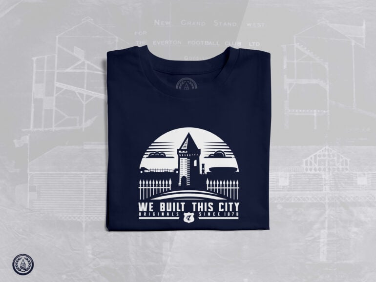 The image shows a folded navy blue T-shirt with a white graphic design on the front. The design features a stylized illustration of Goodison Park, Everton Football Club's historic stadium, with its iconic Archibald Leitch latticework and a prominent tower structure. Above the stadium illustration, there is a semi-circle with a triangular shape at the top, resembling a rising sun or a badge. Below the illustration, the text reads: "WE BUILT THIS CITY ORIGINALS SINCE 1878." The word "ORIGINALS" is in bold, and "SINCE 1878" is smaller, with a small Everton FC crest (a shield with the initials "EFC" and a tower) placed between the two phrases. In the background, there is a faint blueprint or architectural drawing of Goodison Park, with text such as "NEW GRAND STAND WEST" and "THE EVERTON FOOTBALL CLUB LTD" visible, adding a historical and nostalgic touch to the design. The T-shirt is laid flat on a light gray surface.