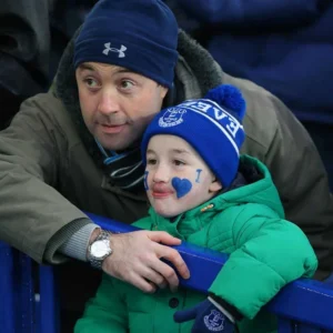 An Evertonian father and child wearing blue club hats at a football match, representing ideas for unique Everton Father's Day gifts.