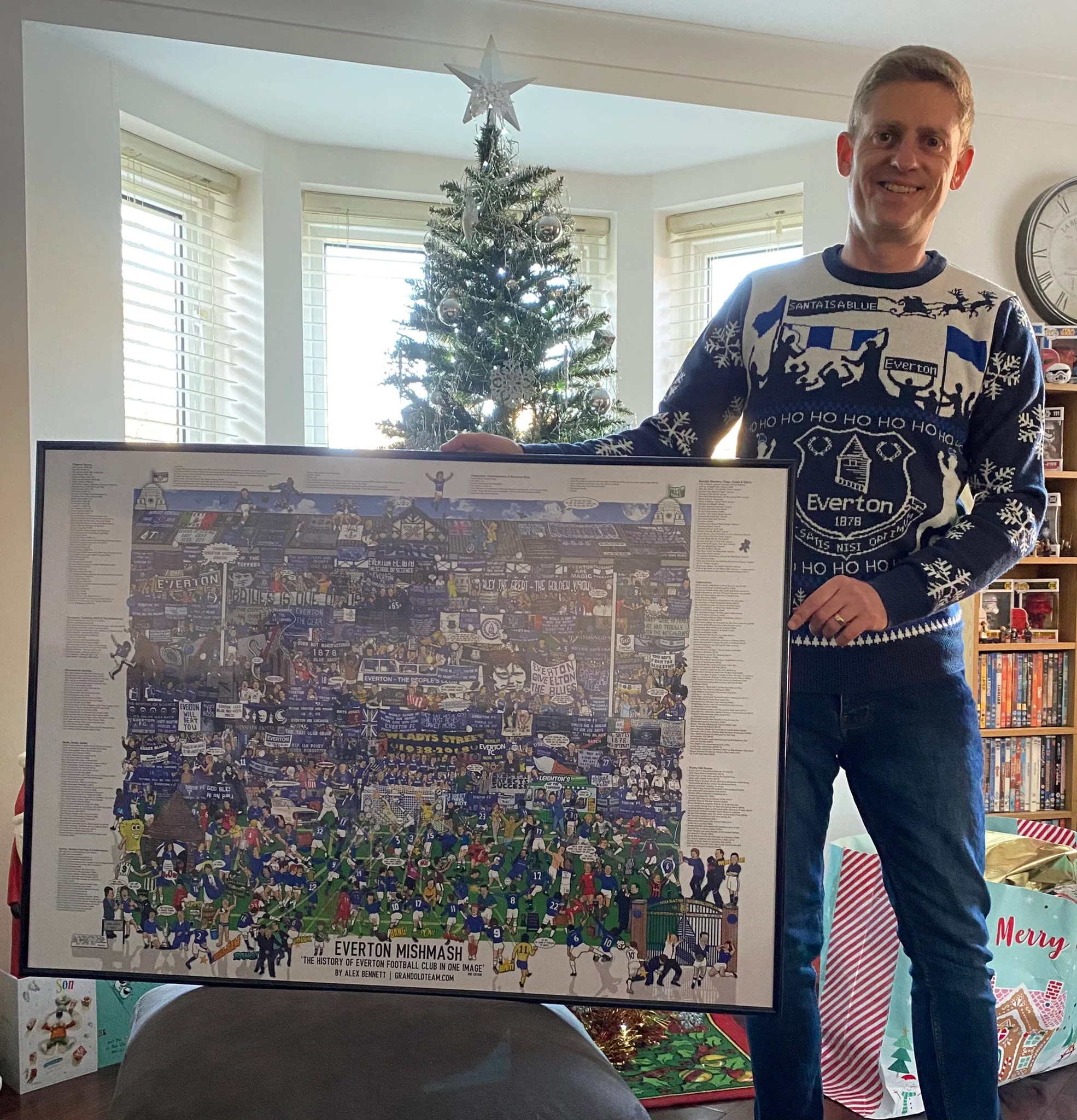 Happy football fan proudly holding a framed Everton Mishmash print, a perfect example of unique Everton Father's Day gifts.